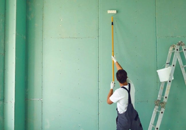 Pintor aplicando imprimación con rodillo sobre placas de yeso laminado en una vivienda de obra nueva