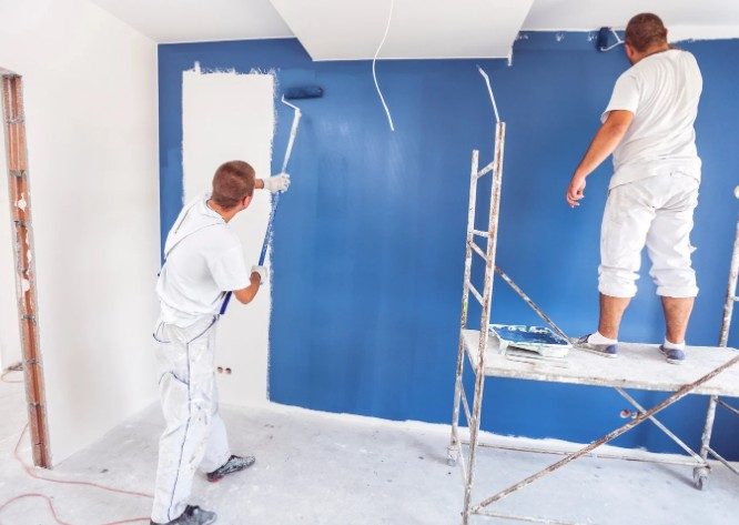 Dos pintores aplicando pintura azul corporativa en la pared de una oficina en Vigo