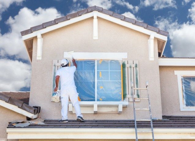 Pintor protegiendo las ventanas de un chalet antes de pintar la fachada y los aleros