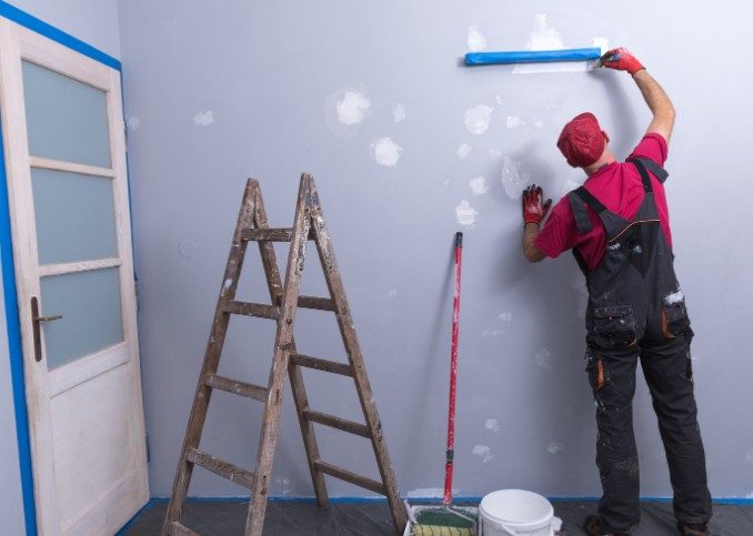 Pintor lijando y repasando la masilla aplicada sobre las grietas de una pared antes de pintarla