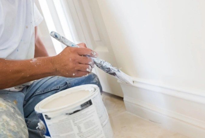 Pintor cortando con brocha el esmalte blanco en el rodapié y la carpintería de una vivienda