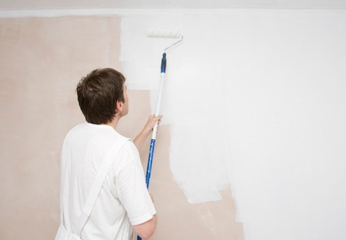 Pintor cubriendo con rodillo una pared manchada tras el tratamiento de humedades en una vivienda