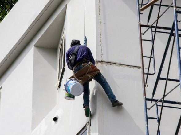 Pintor trabajando en altura sobre la fachada de un bloque de viviendas junto a un andamio